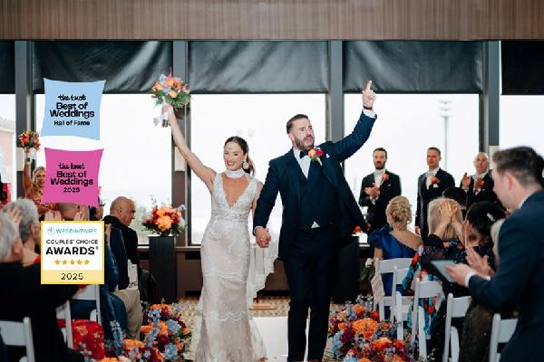 Newlywed couple walking down the aisle, raising their arms in celebration as guests applaud.